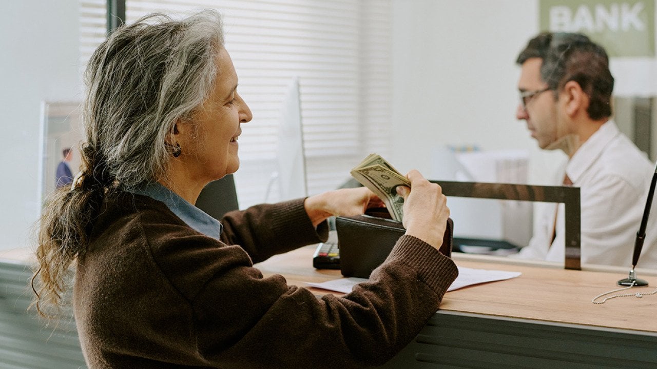 A senior woman handing money to a bank teller.