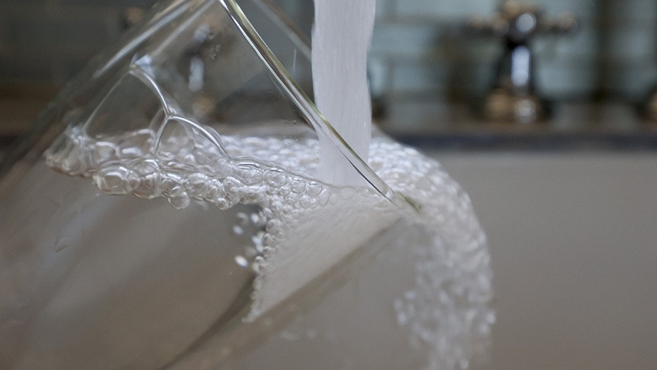 Water running from a kitchen faucet to fill a glass.