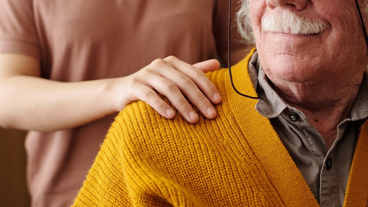 A young adult patting the shoulder of an elderly person as care and support.