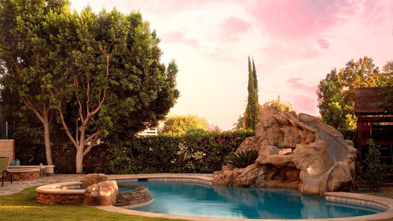 A modern backyard pool with rock waterfalls and slide.