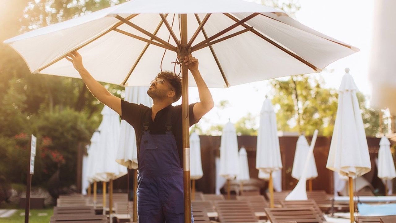 A hotel officer setting up a parasol beside the hotel's pool before guests' arrival.