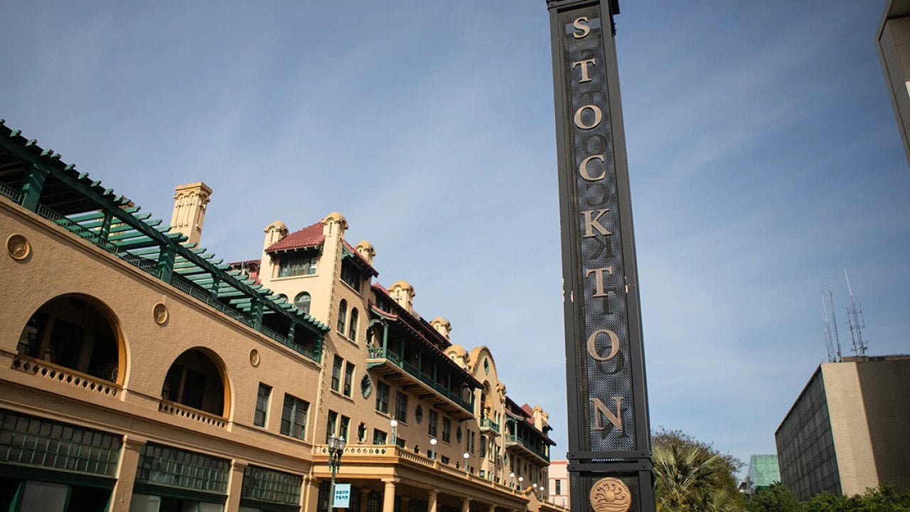 View of a street in downtown Stockton with a tall metallic sign with the city name vertically displayed in 2026.
