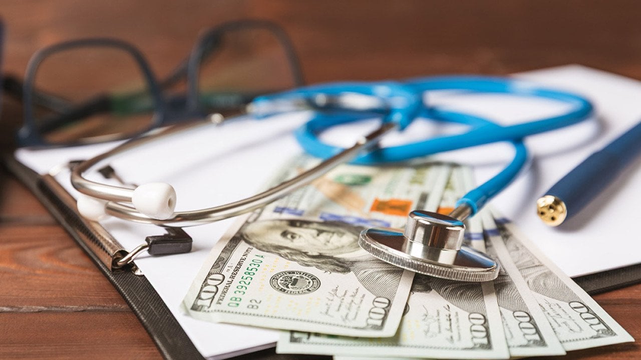 U.S. dollar bills, medical records, and a stethoscope placed in a desk.