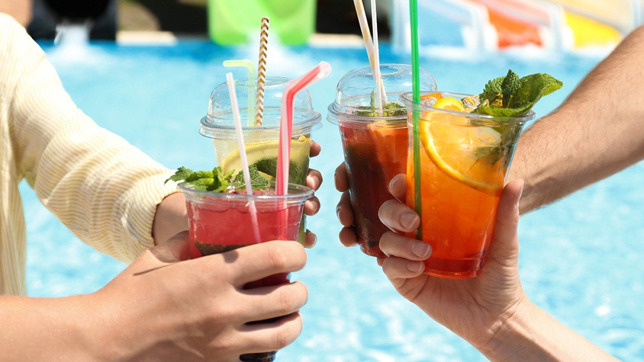 A group of friends putting up their drinks together beside a pool.