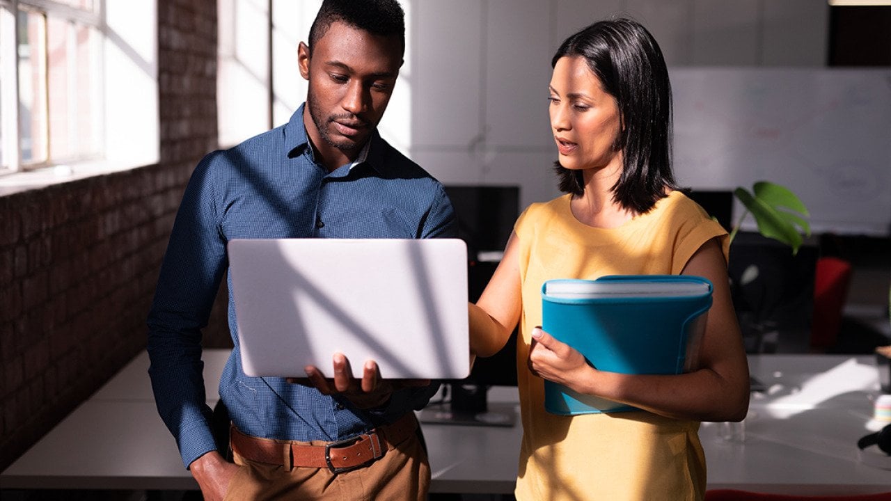 Two colleagues standing in an office discussing a task together.