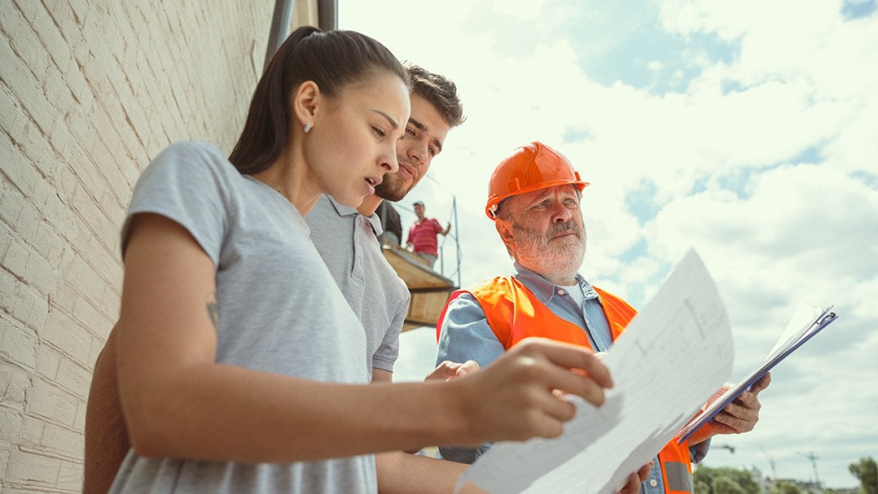 A foreman showing a young couple the plans to their new home.