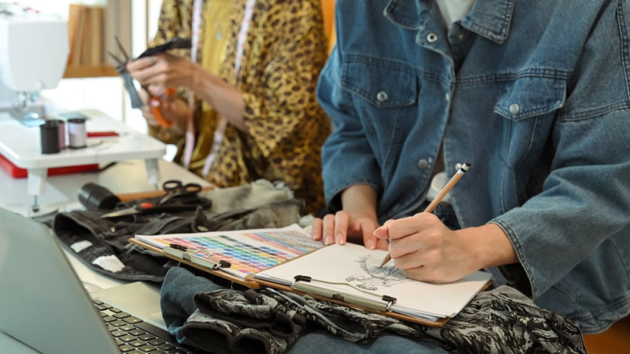 Fashion designers sketching and crafting new clothing designs in their studio.