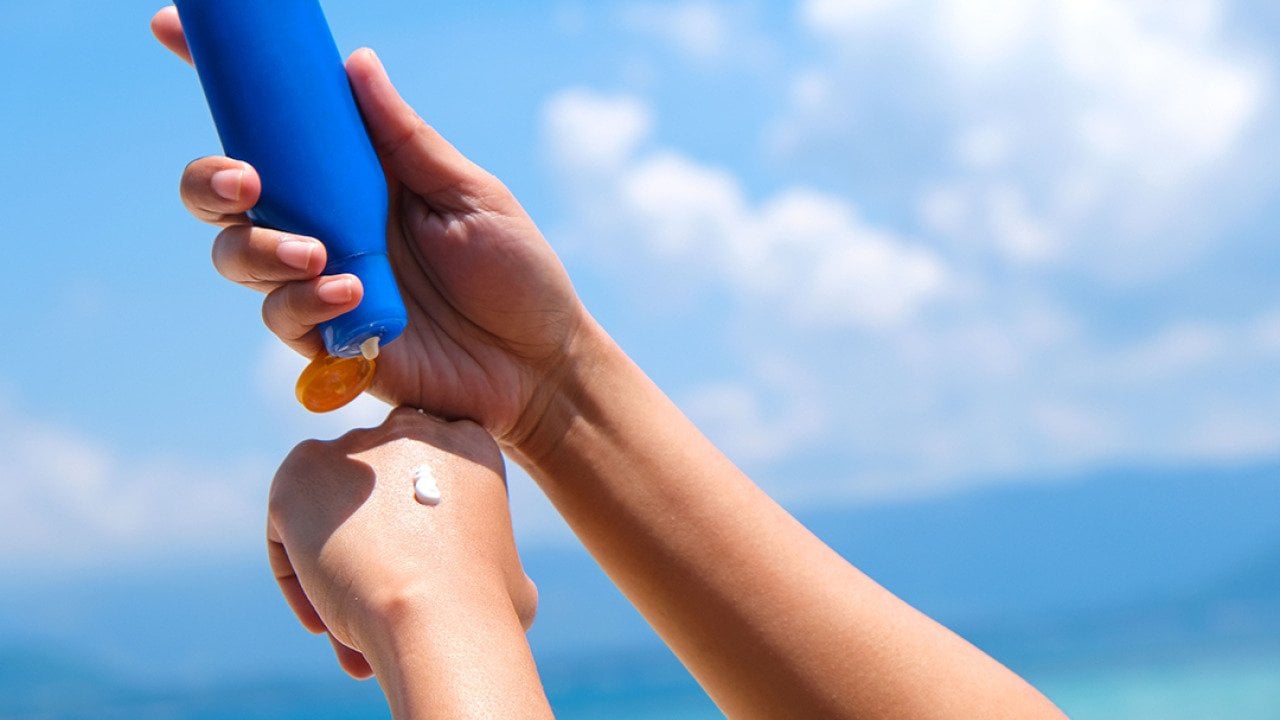Person putting sunscreen under the sun while at the beach.