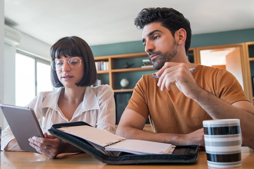 A young couple reviews and pays bills online using a digital tablet.