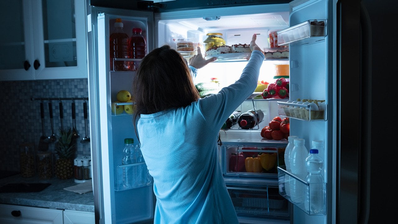 Woman storing food in the refrigerator at night.