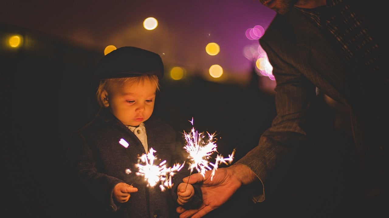A father helping his young child with sparklers during a New Year celebration.