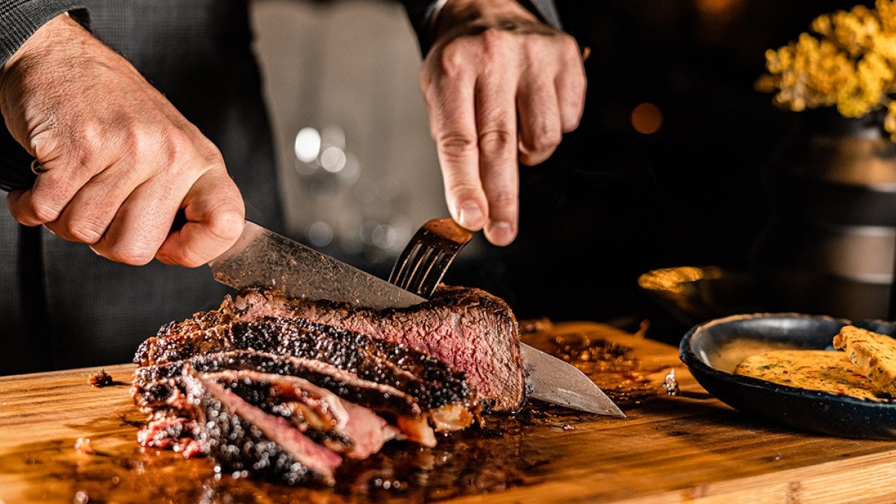 A butcher slicing a tomahawk steak in a serving table for a customer in a steakhouse restaurant.