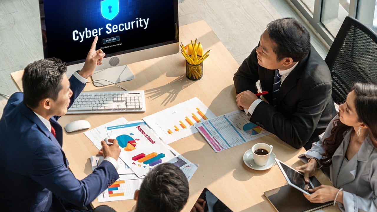 A group of business executives discussing cybersecurity as seen from a monitor.