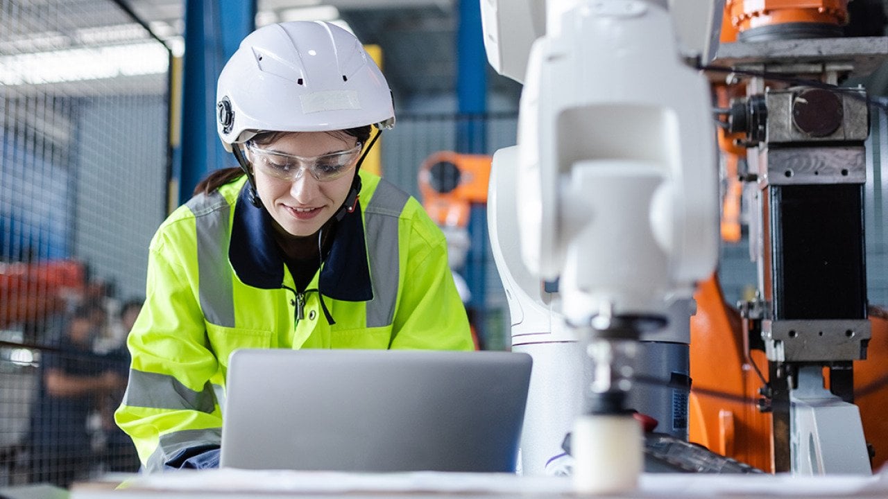 An engineer checking automation robotics from a laptop for a manufacturing machine in an industrial factory.