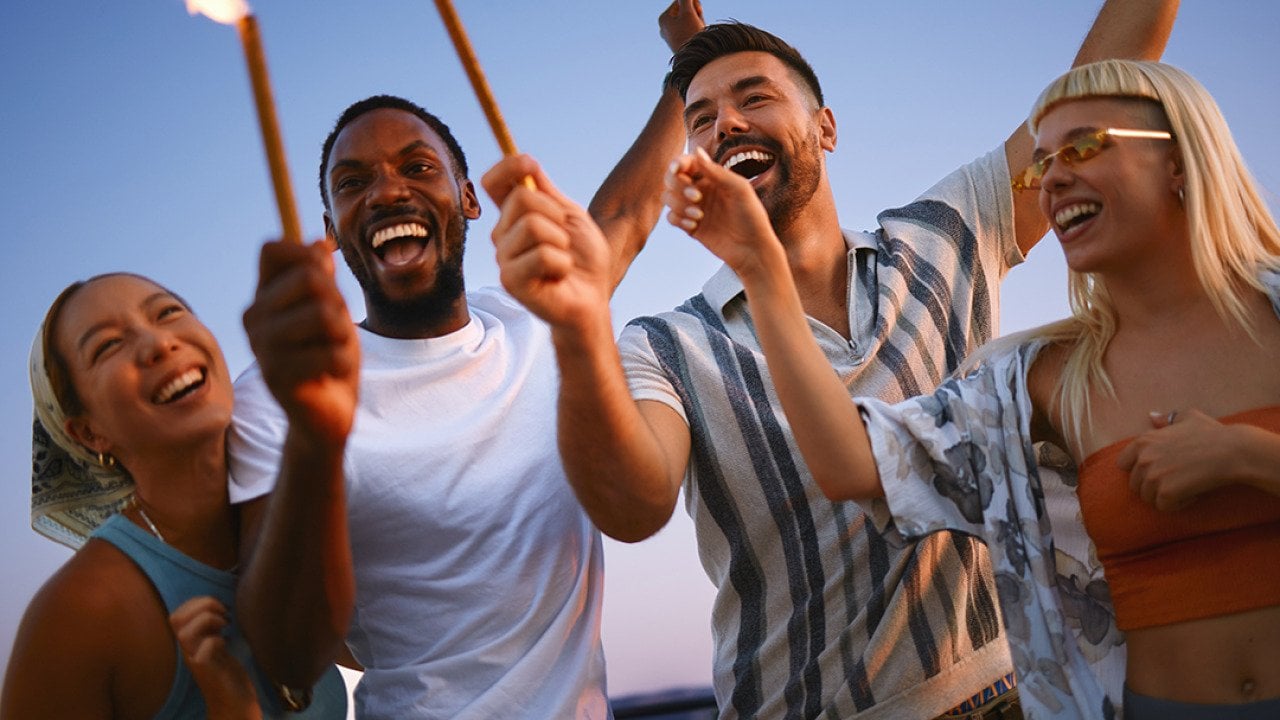 A group of friends celebrating together with sparklers during a rooftop party at sunset.