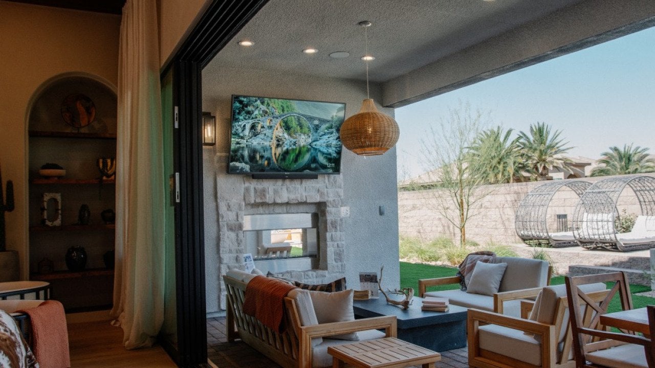 A modern covered patio in a backyard with extended living area, outdoor television, and fireplace.
