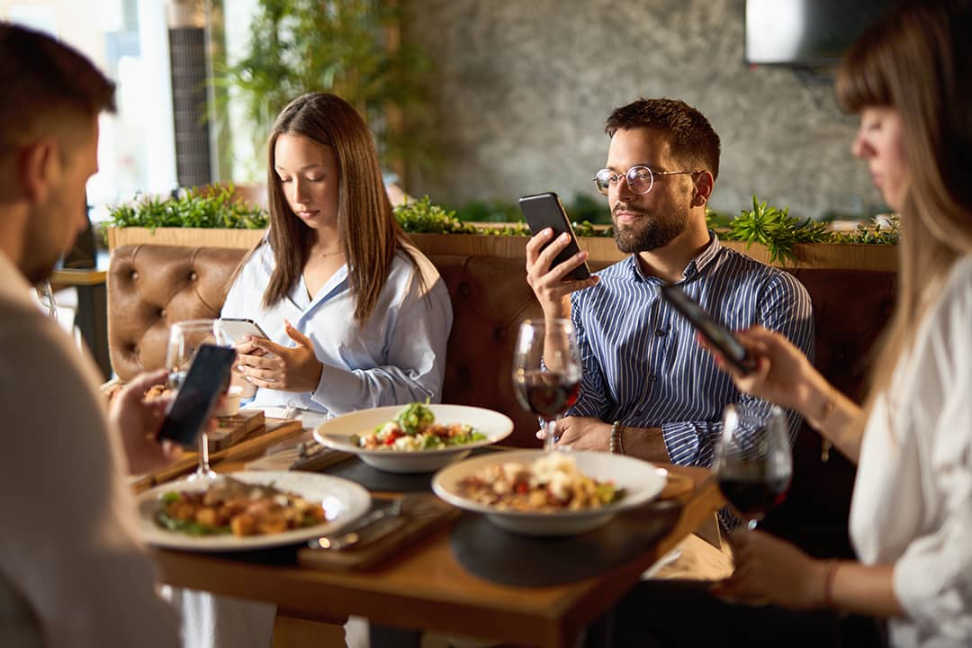 A group of business colleagues checking their smartphones while eating lunch in a restaurant.