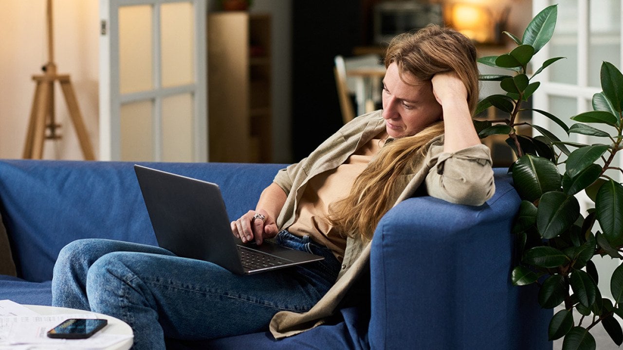 A stressed young woman at home looking at taxes from a laptop.