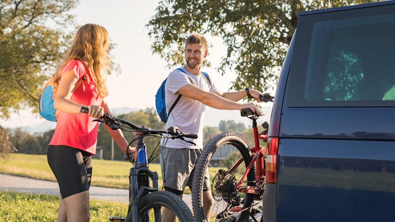 A couple taking down electric mountain bikes from their van for a nature recreational adventure.