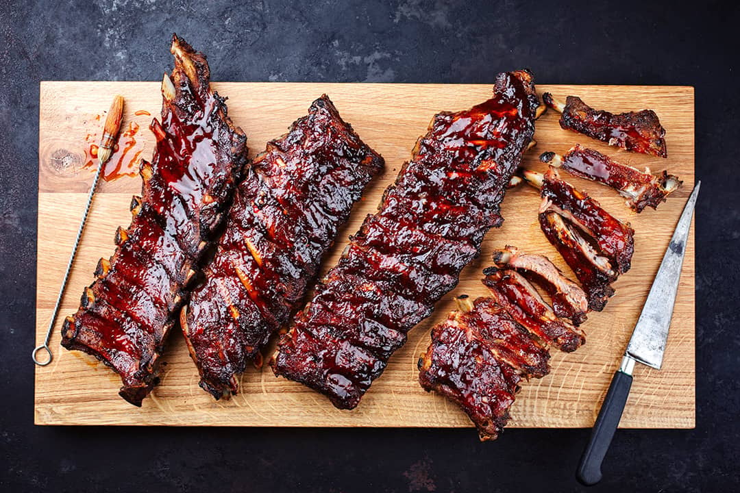 Slabs of freshly barbecued ribs sliced on a wooden cutting board.