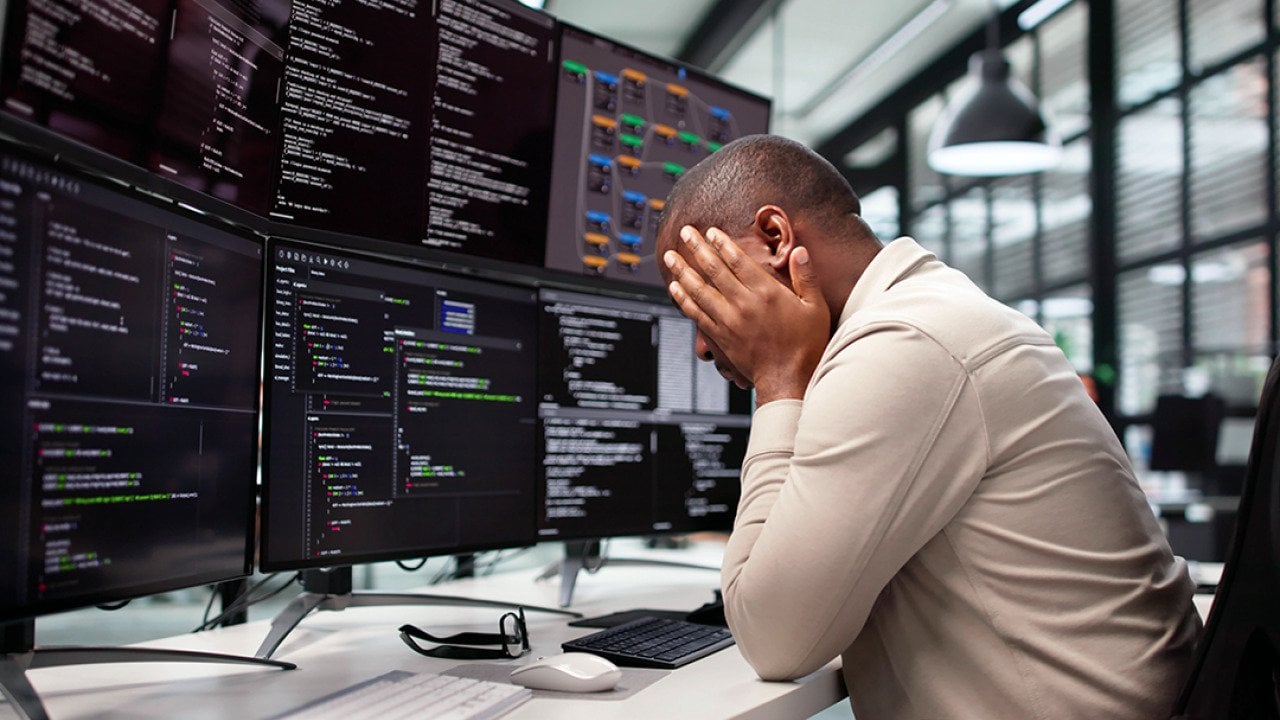 A stressed programmer at work facing multiple monitors.