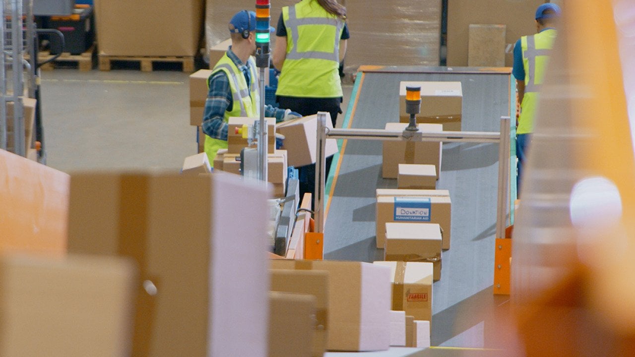 A logistics team in a warehouse working along a conveyor belt to sort and load packages.