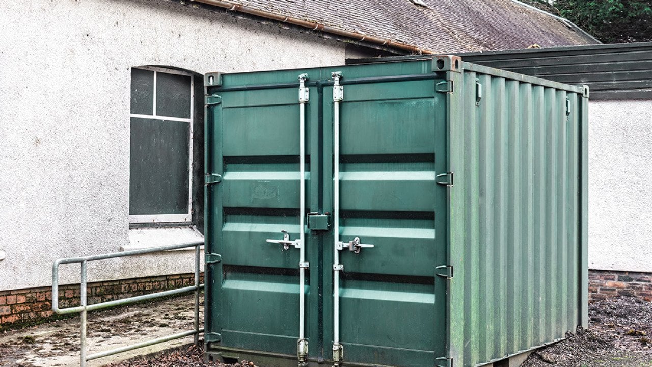 A large steel storage container positioned outdoors beside a building.