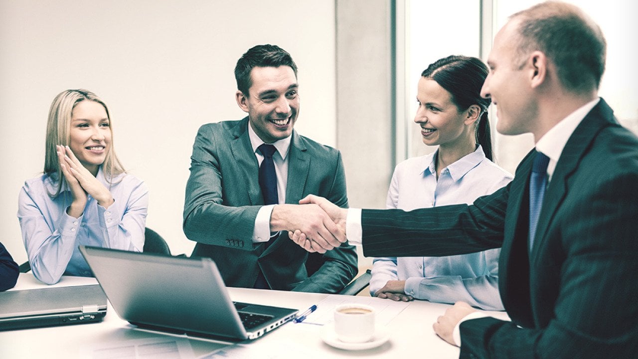 A business team with its two leaders shaking hands during a meeting.