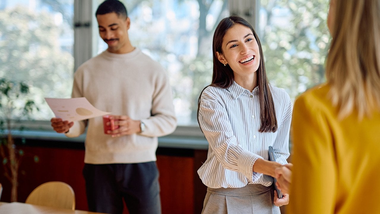 A businesswoman enthusiastically shaking hands with a new coworker.
