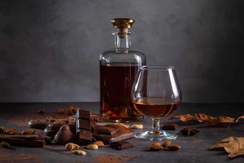A glass of cognac, cognac in a bottle and pieces of chocolate on a dark background.