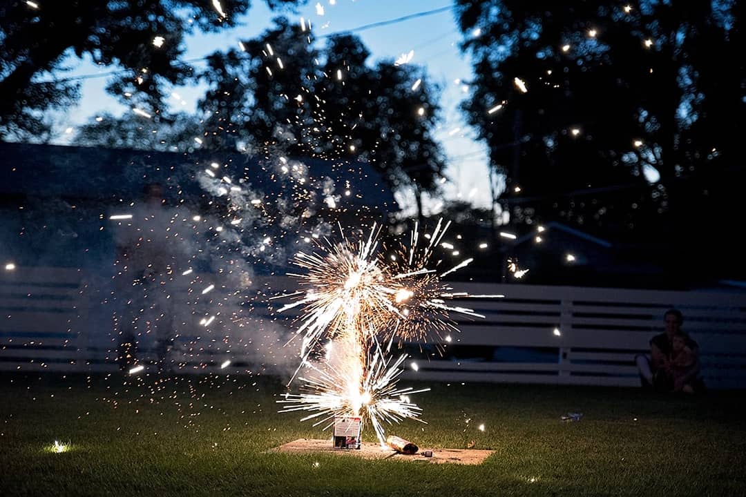 Fireworks going off at a backyard picnic during Fourth of July.