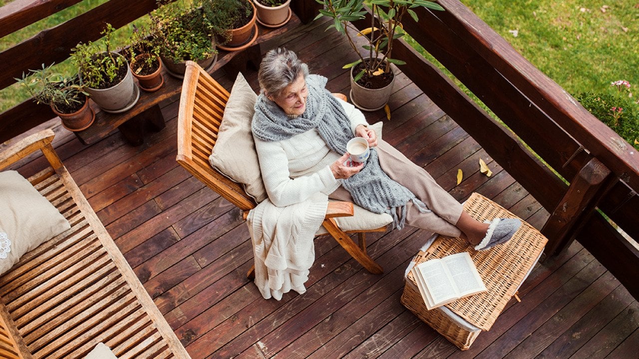 Top view of an elderly woman with a book while sitting relaxingly by her home's terrace.