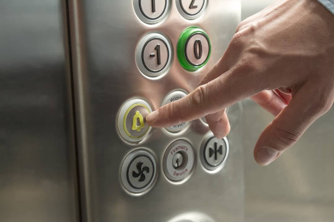 A person's hand pressing the alarm button in the elevator.