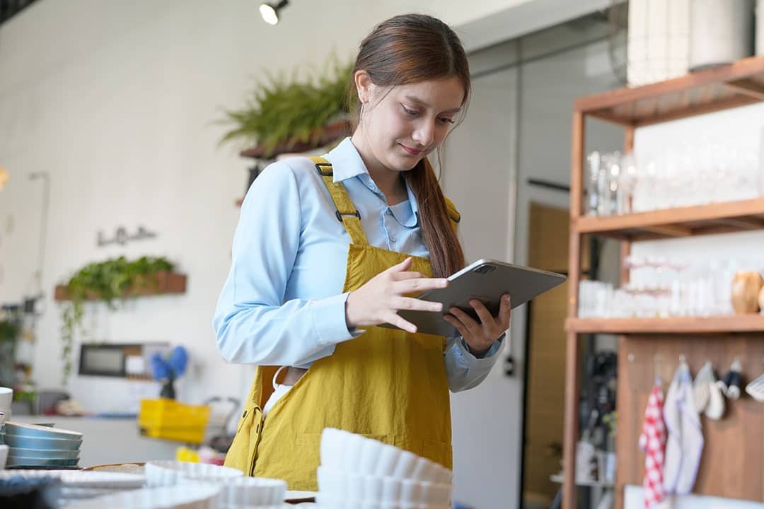 A shopkeeper checking inventory stocks of pottery and tableware from a work tablet device.