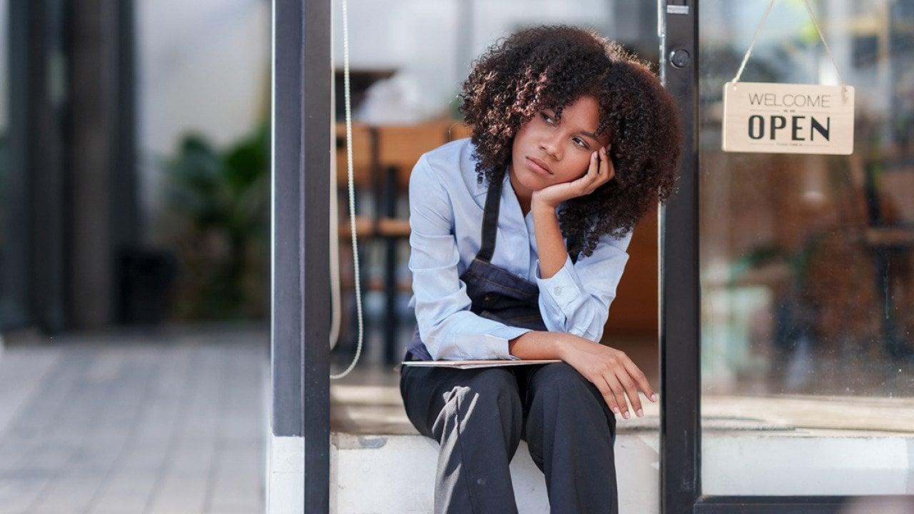 A female shopkeeper stressfully sat outside her store.