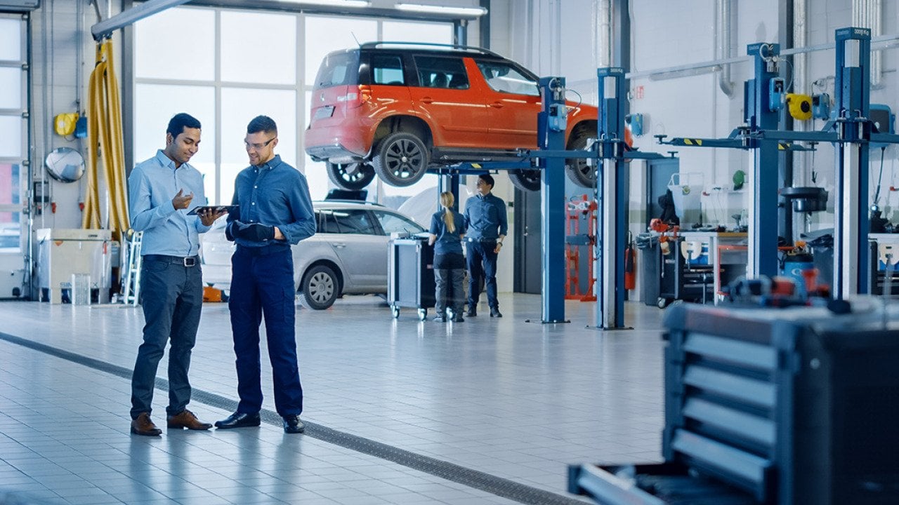 A manager explaining diagnostics results and vehicle breakdown to a mechanic in a car workshop.