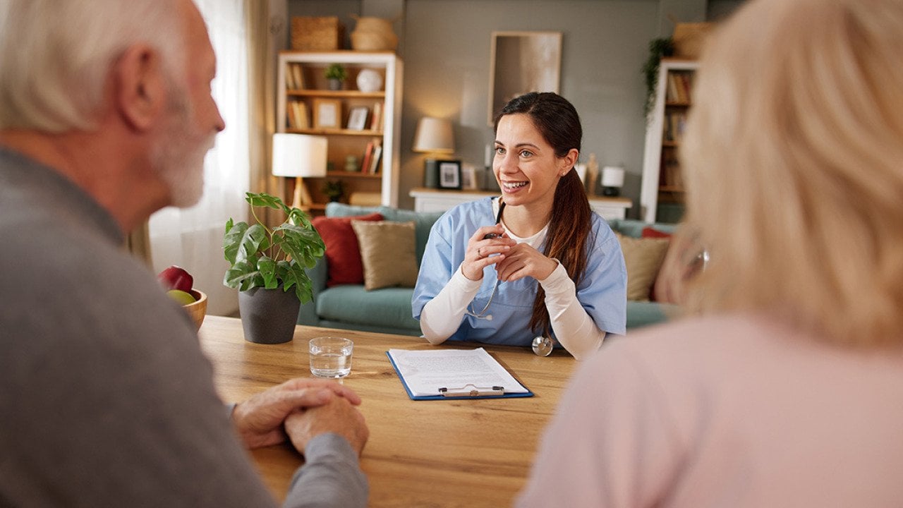 A nurse discussing health issues and plans to elderly patients during a home visit.