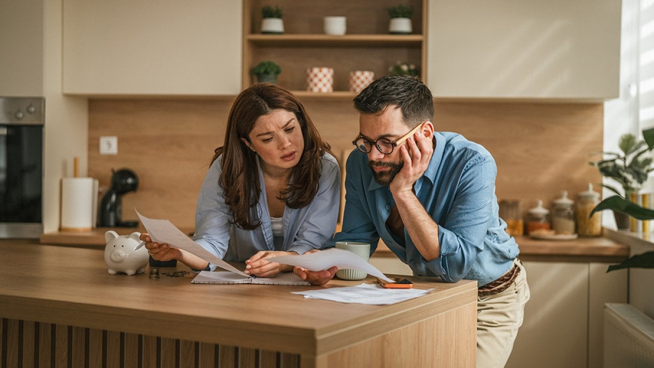 A couple reviewing bills and documents from their household finances at their home's kitchen.
