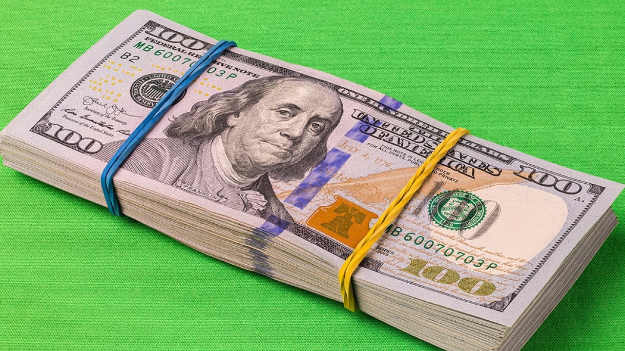A pack of 10,000 U.S. dollars laid on a striking green background.