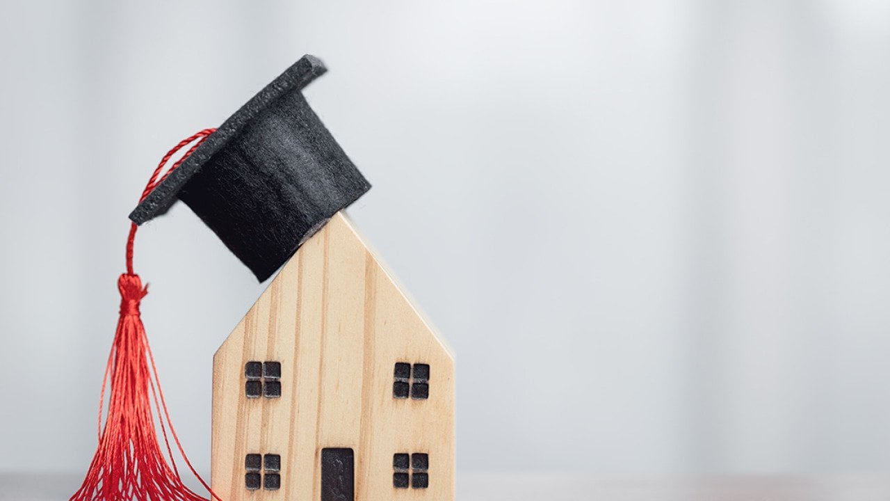A miniature figures of a graduation cap on a wooden house, symbolizing the concept of success in education.