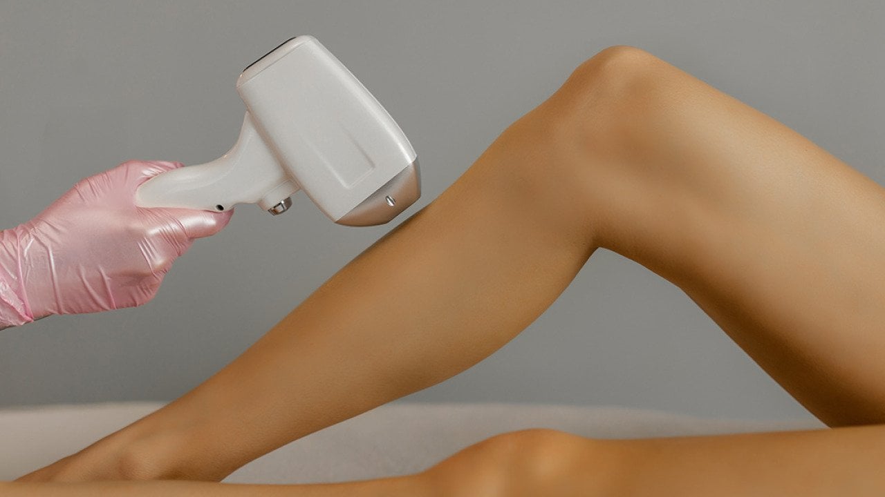 A cosmetologist doing hair laser removal to a patient's leg in a beauty salon.