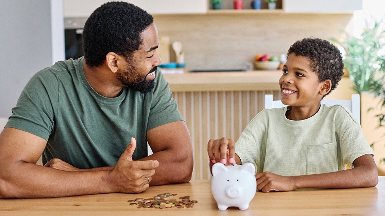 A father teaching his young son to save money in a piggy bank.
