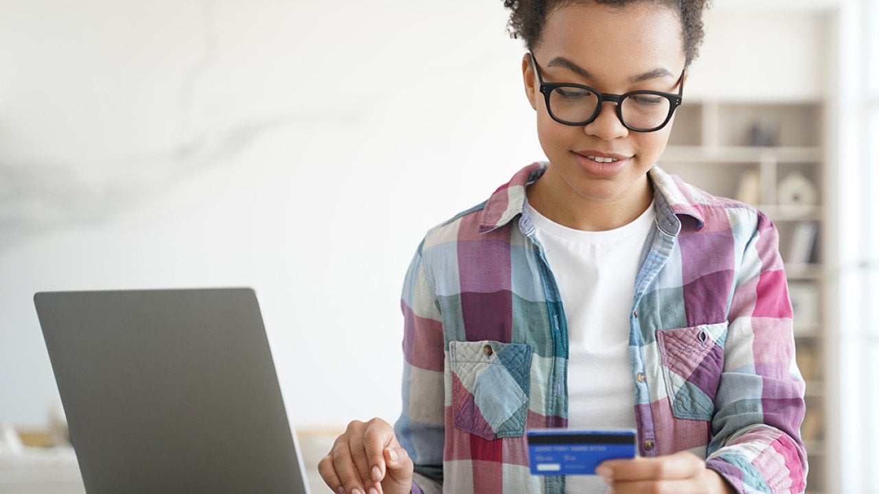 A teenager holding a credit card while shopping online from a laptop.