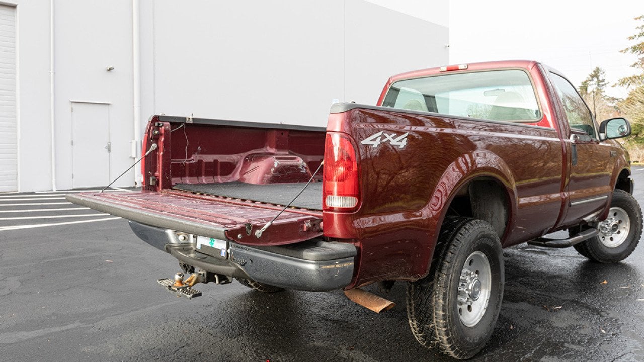 A burgundy 2000 Ford F-250 Super Duty pickup truck parked in an outdoor garage with its tailgate open.