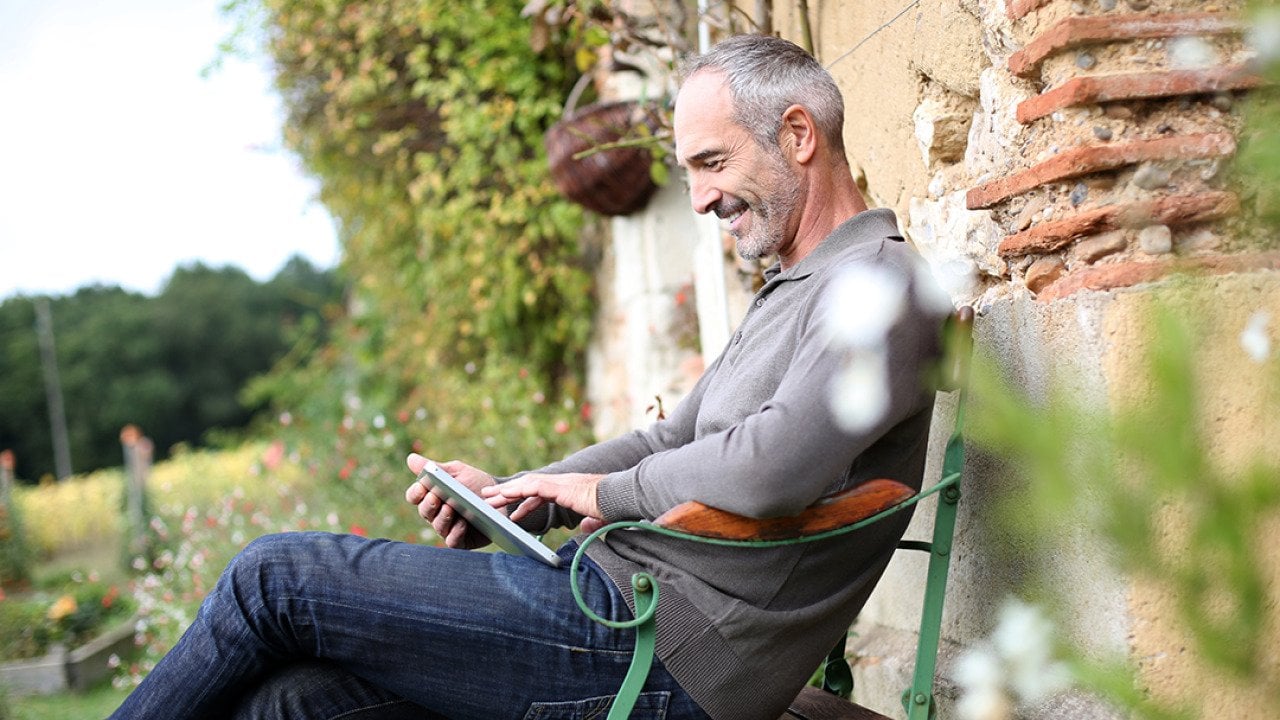 A middle-aged man using phone while sitting on a bench in a countryside home.
