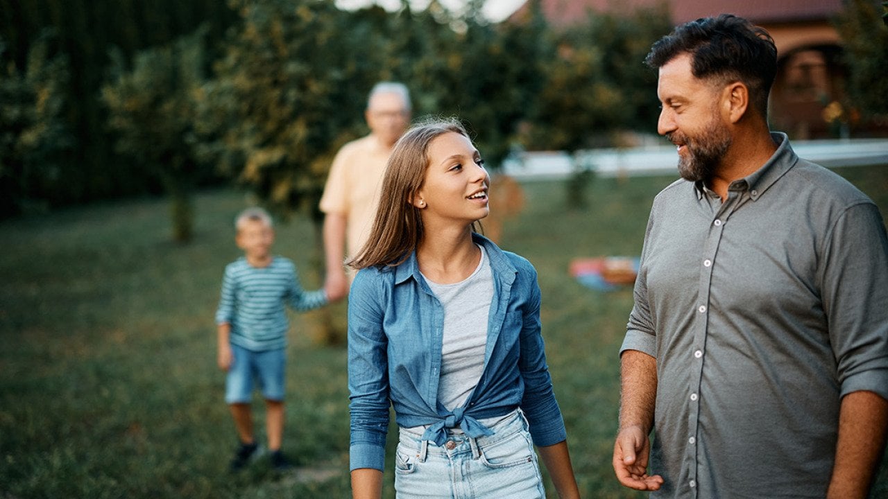 A teenager sharing stories with her father, while walking in the backyard with the family.