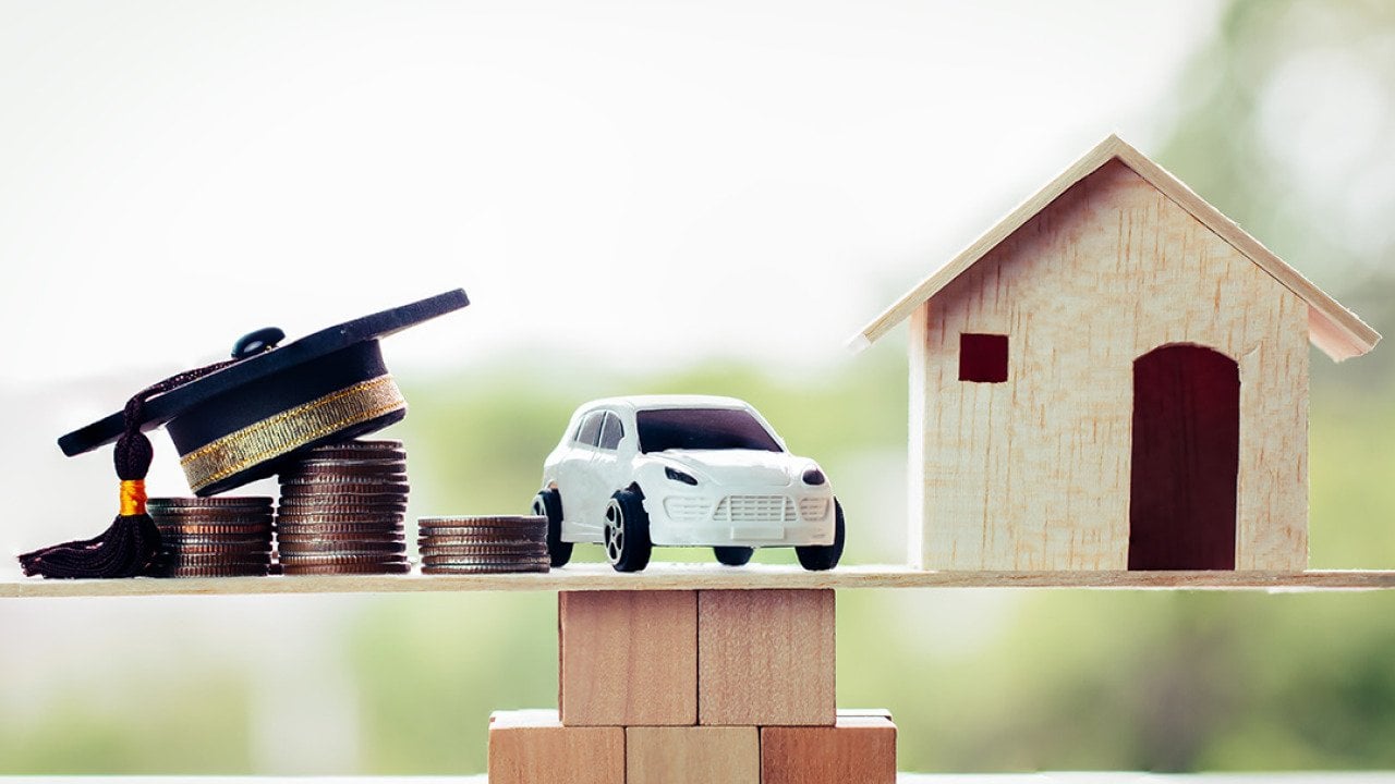Miniatures of a graduation cap on top of coin stacks, a car, and a house above a wooden block, symbolizing the concept of success in university education.