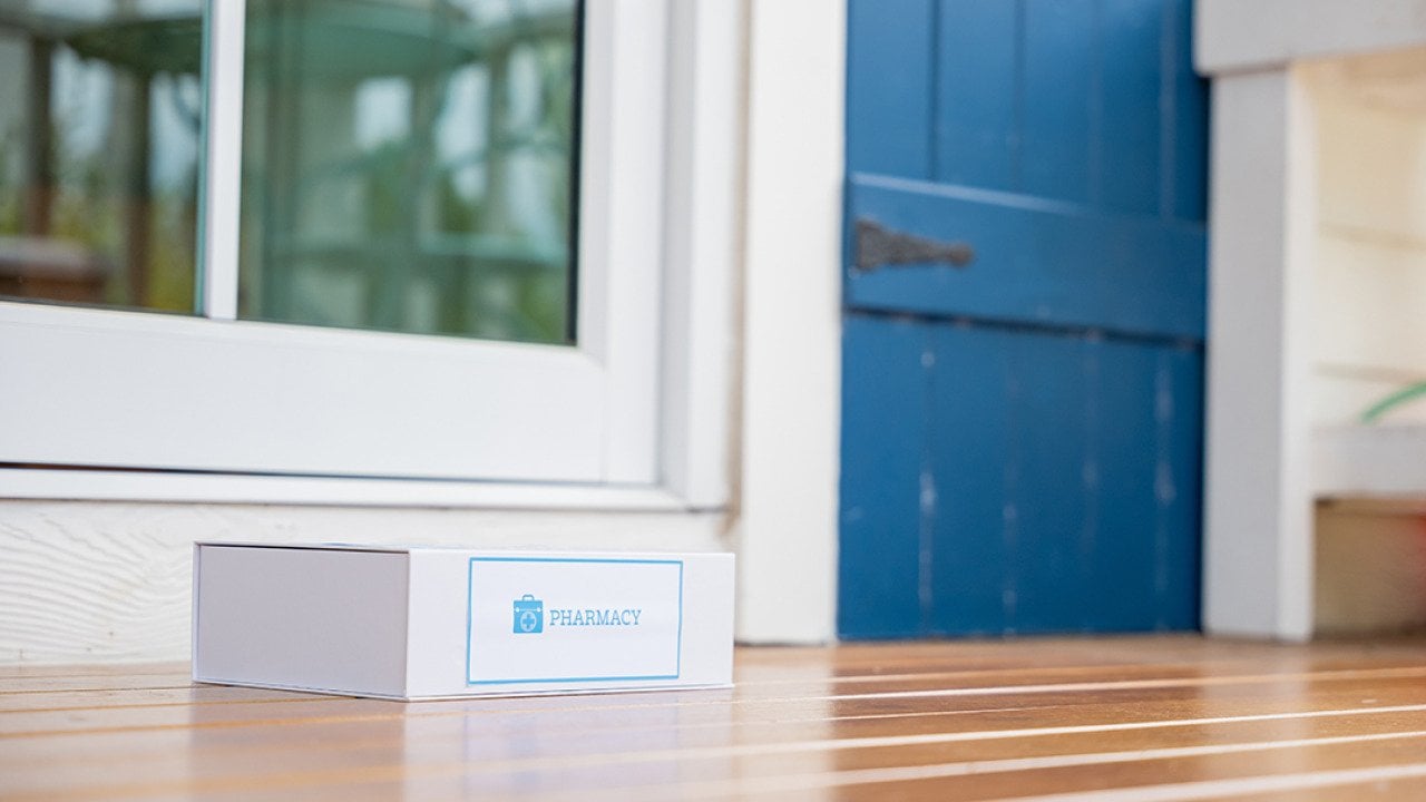 A package box labeled from pharmacy left on the front porch of a house as a delivery.