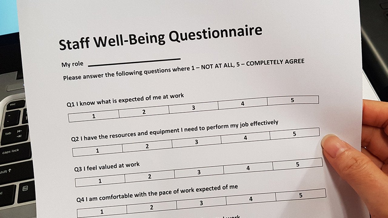 A staff well-being questionnaire held by a person's hand. 