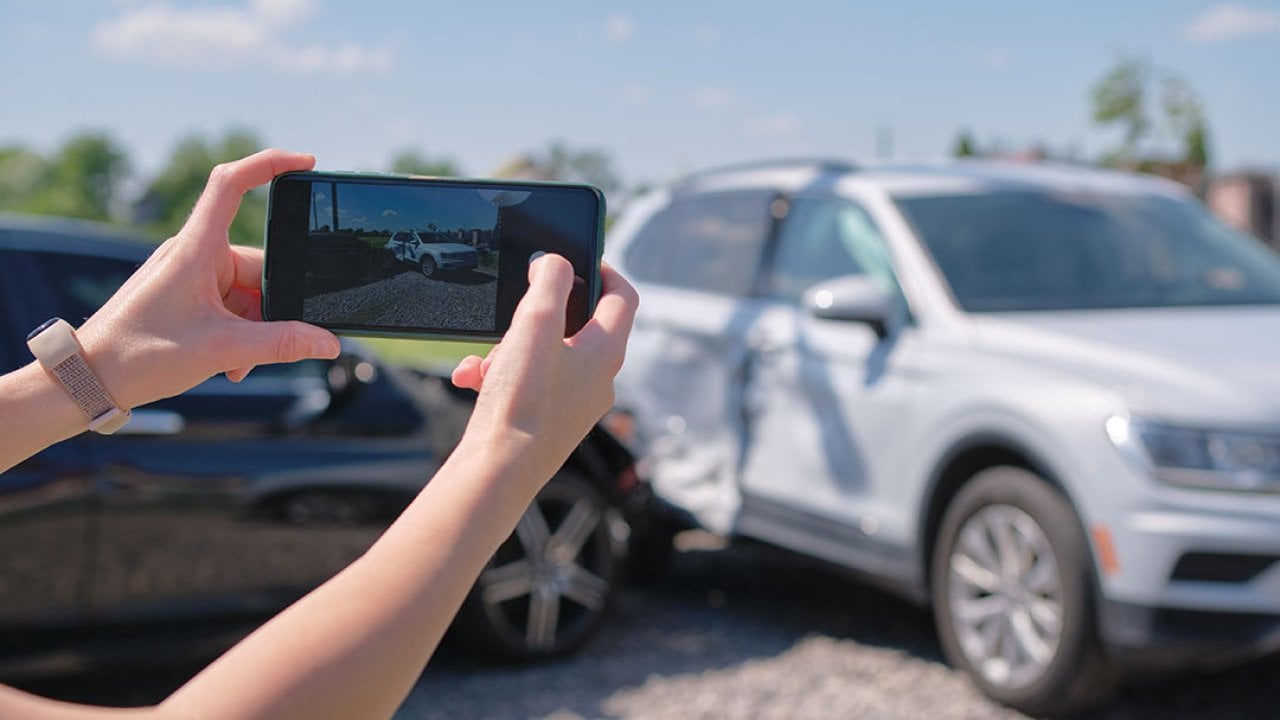 A driver taking a photo of their car's damage after an accident.